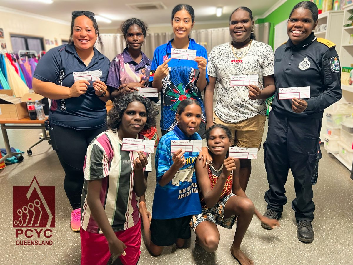 Eight woman from Arukun PCYC are smiling ar the camera holding FIFA world cup tickets. Pictured is six kids from the PCYC along with the communinities youth support worker and police liason officer.