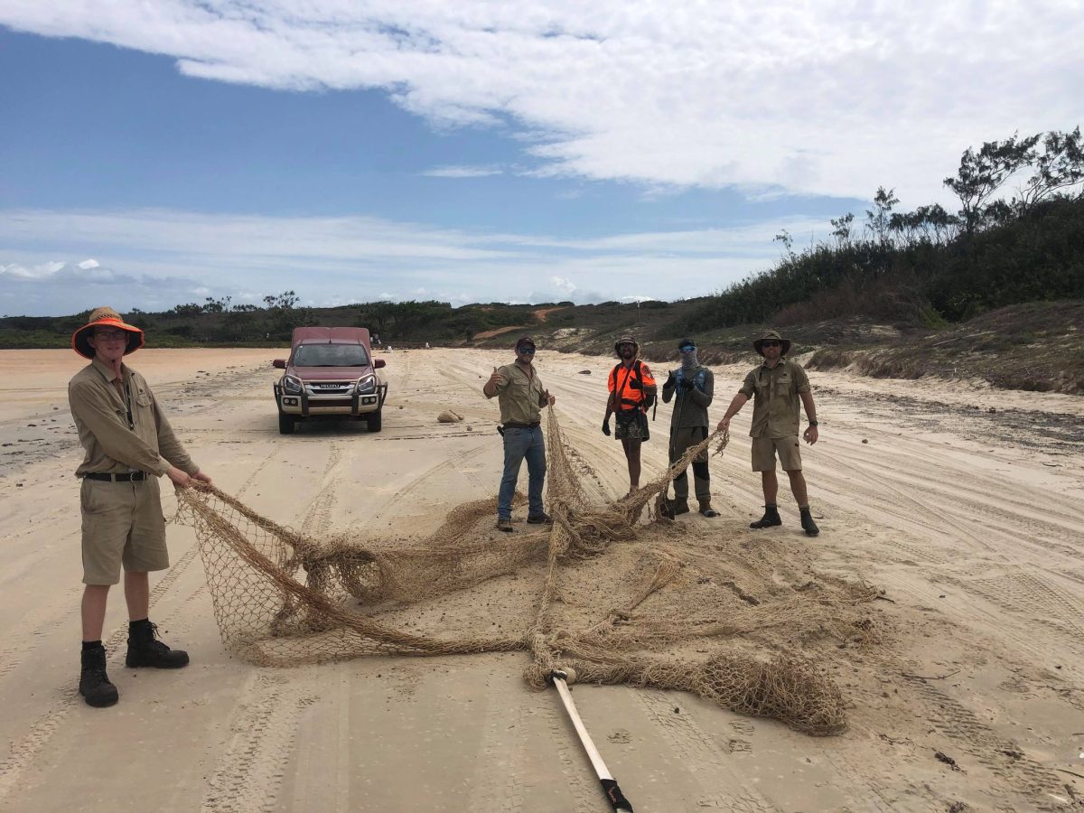 Pictured are five rangers on a dirt road holding a commercial fishing net.