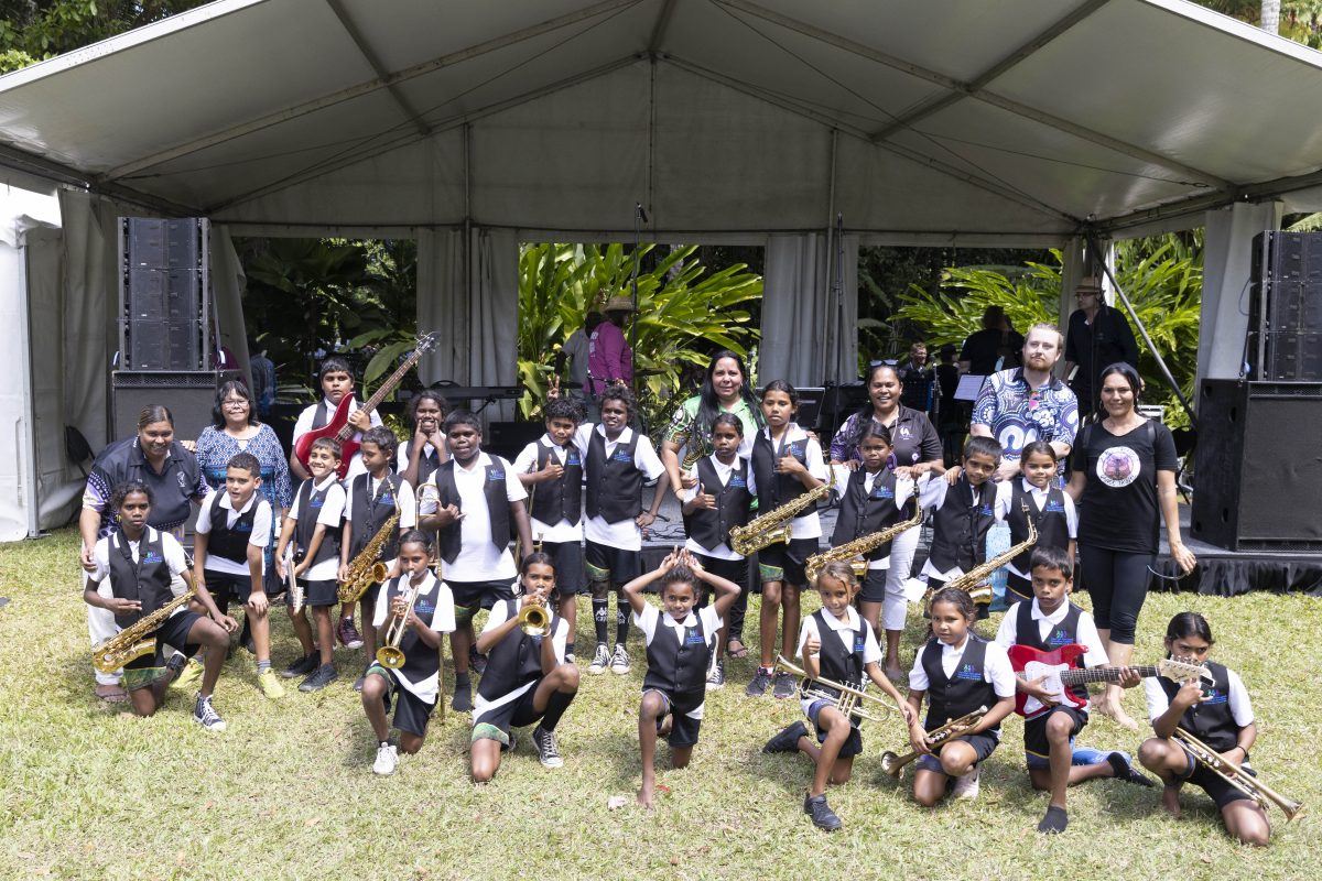 Group photo in front of the Cairns Festival stage featuring Auntie Dora, the Red Dirt Band and students from the Cape York Aboriginal Australian Academy.