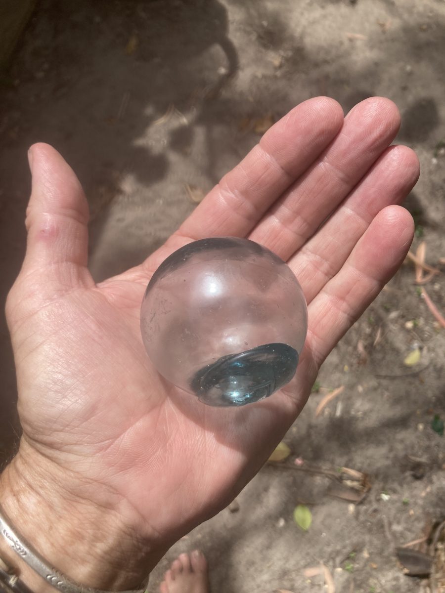 Pictured is a hand holding out a miniature glass buoy which is about half a palm size.