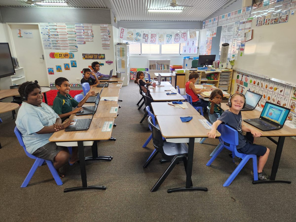 Students sit at their desks with laptops open in front of them.