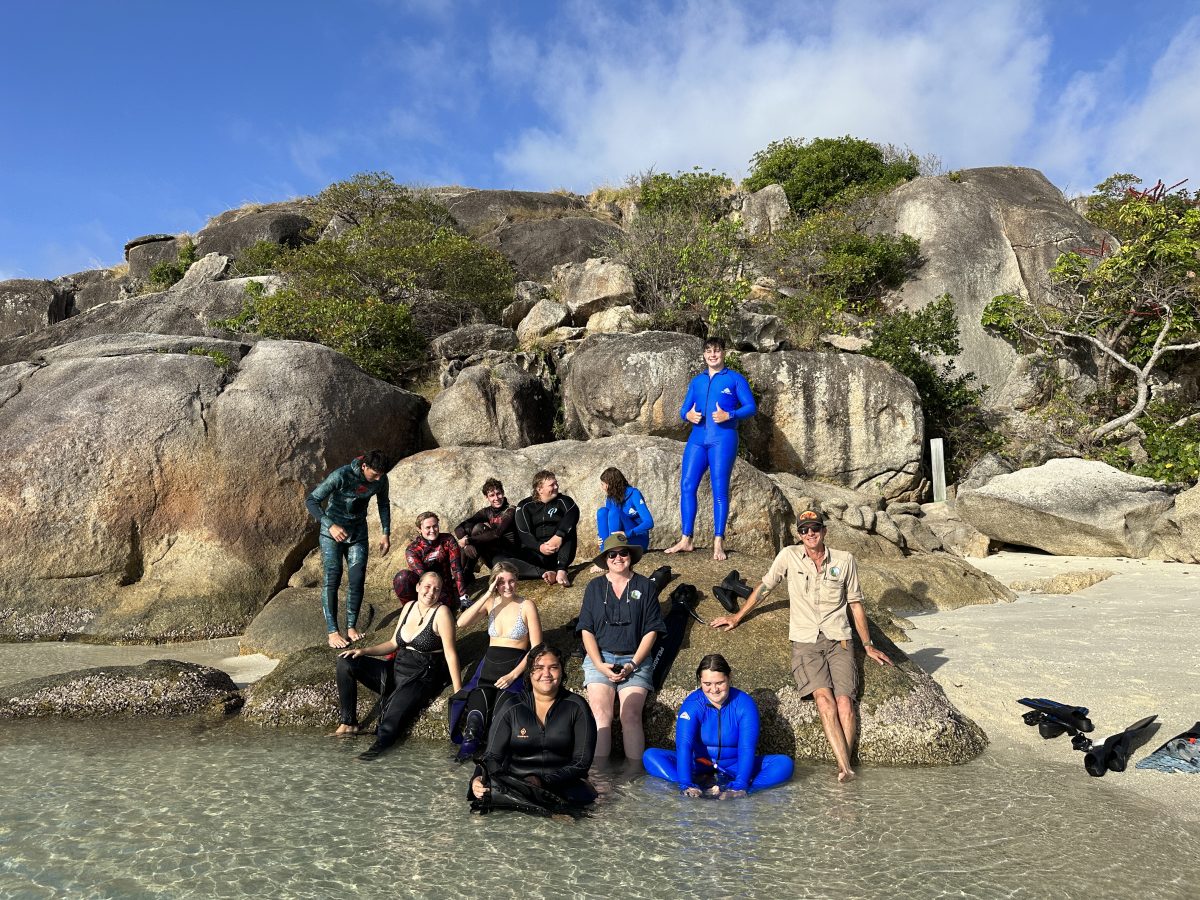 The group sits on big rocks by the water before diving in for their first snorkelling afventure of the trip.