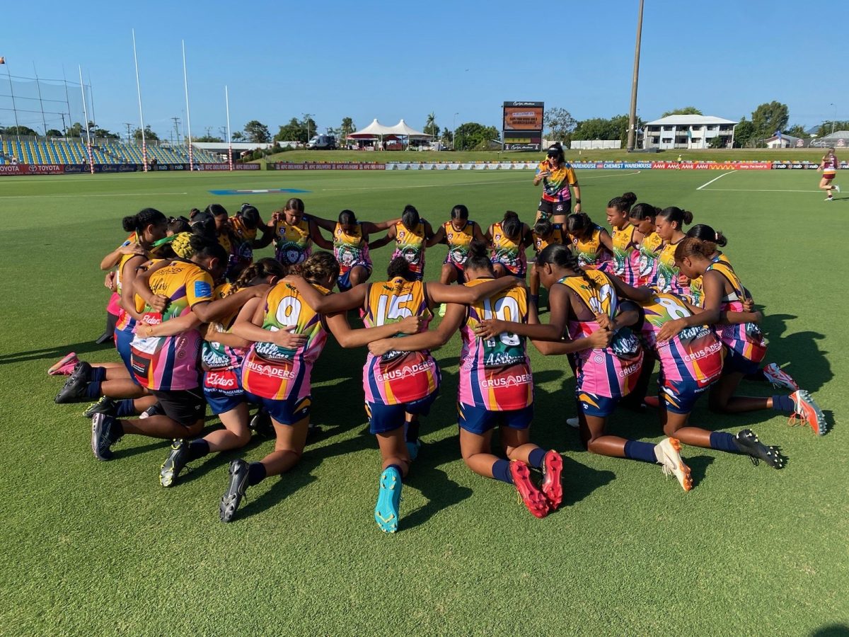 Australian rules women's team kneeling down in a circle on the field