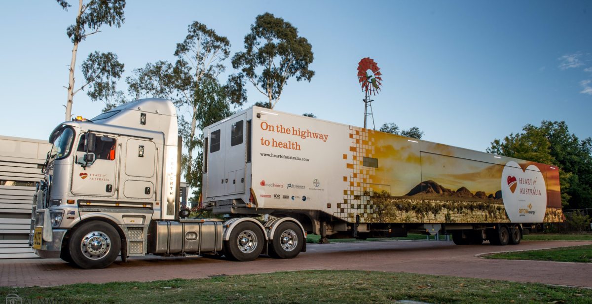 A big truck with "Heart of Australia" written towards the back and "On the highway to health" towards the front is parked.