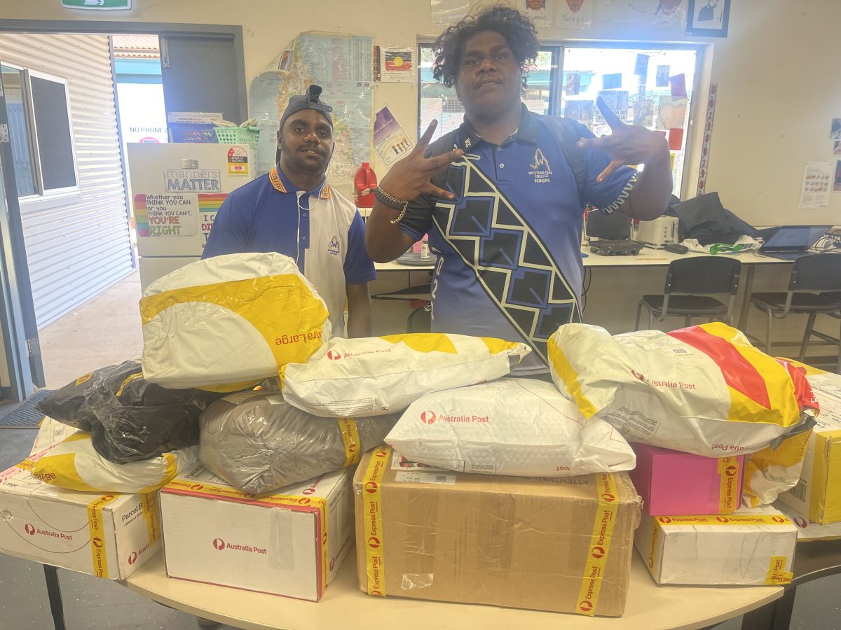 Two students in Western Cape College uniforms are standing behind a table that is has multiple parcels piled on top.