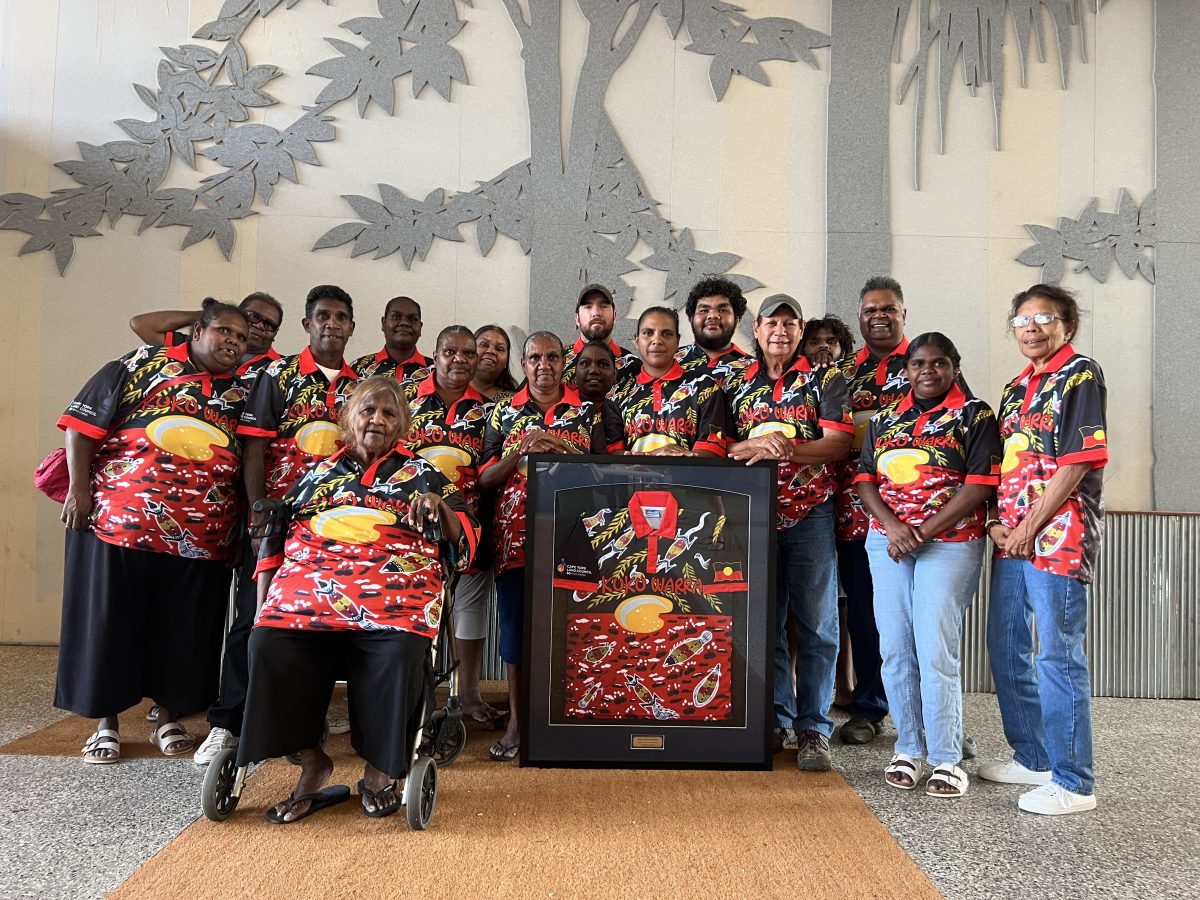 Group picture of the Kuku Warra peoples dressed in red, black and white shirts with Kuku Warra written on them.