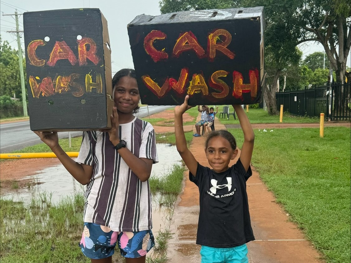 Young child and older youth hold up car wash signs