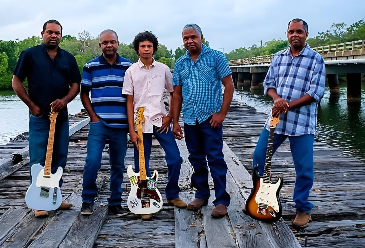 Five-member band with three guitars on a wharf.