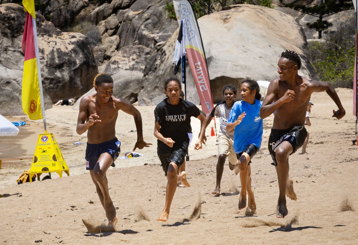 Five young runners race on the beach.