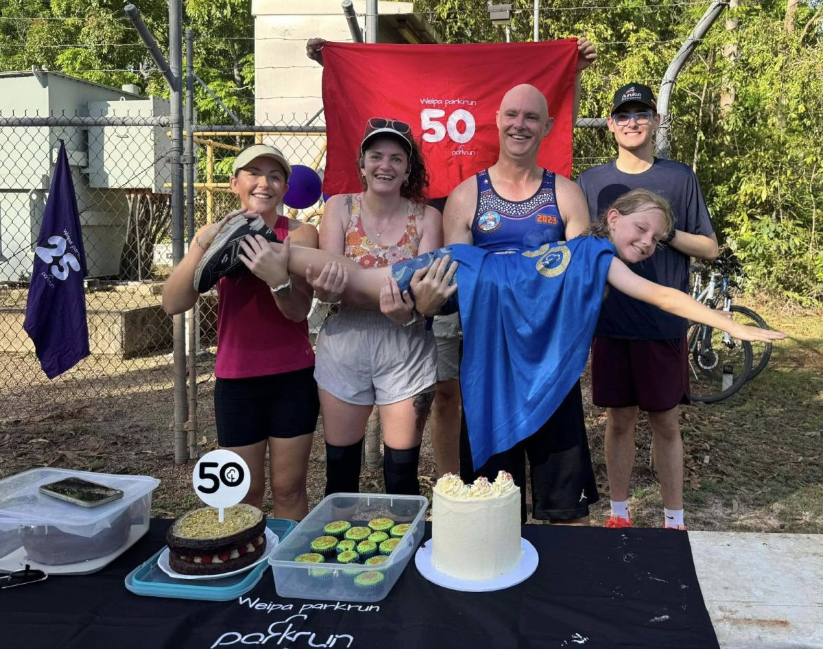 Four runners hold a younger runner in Superman pose.