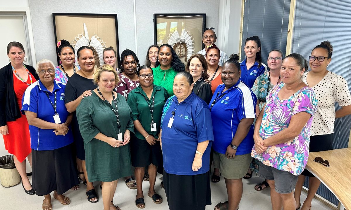 One person stands at the forefront of a group of 18 people also standing.