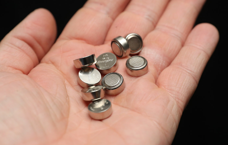 Nine button batteries held in the palm of a hand.